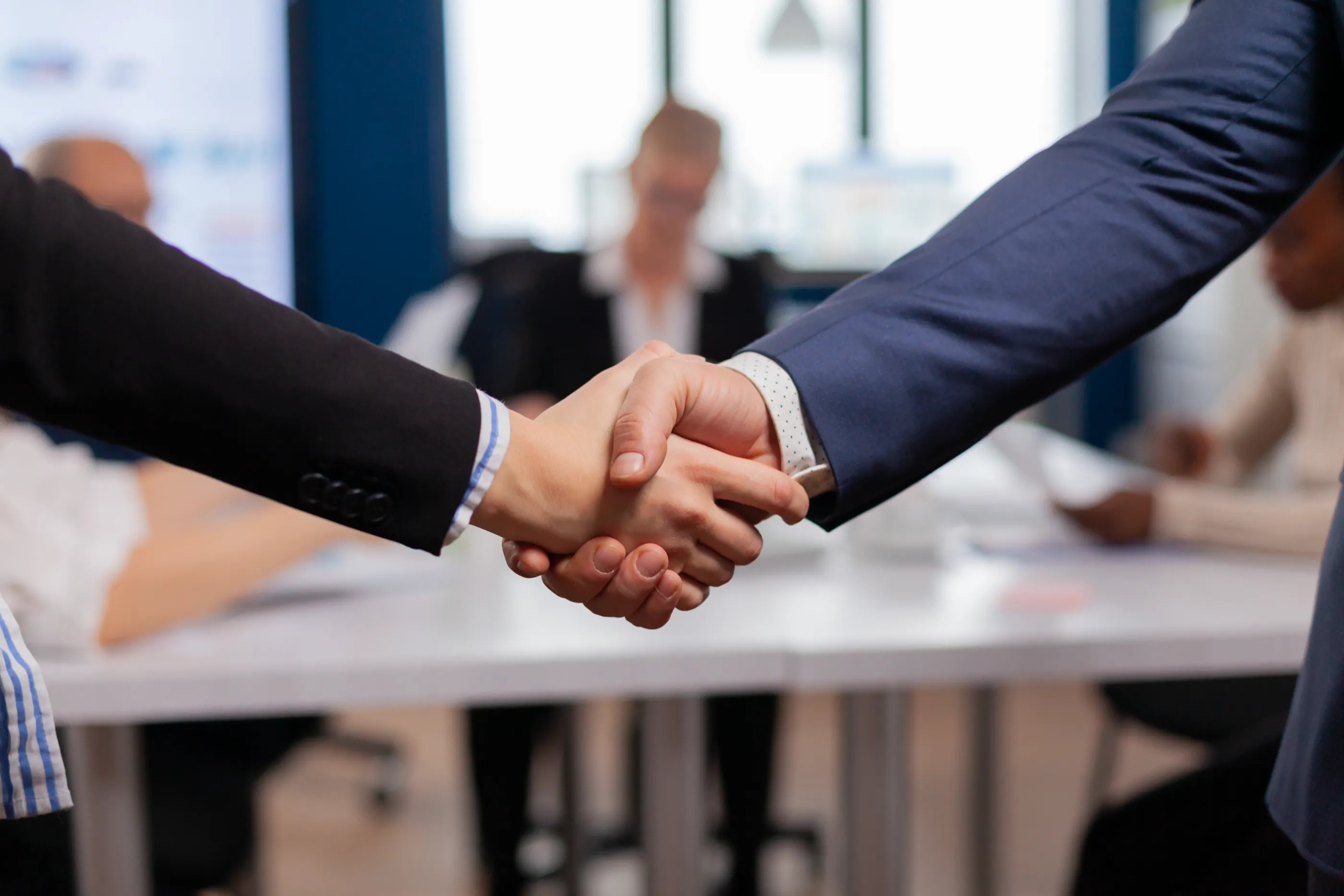 A manager and a new hire shaking hands across a meeting table